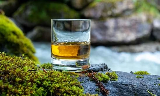 Whisky Lowlands Glas Laowland Whisky neben Heidekraut vor Fluss